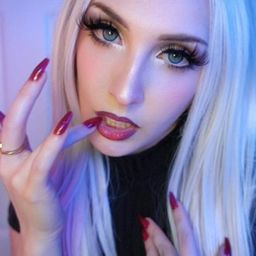 Matriarch Malice looking directly into your eyes with her nail touching her lips